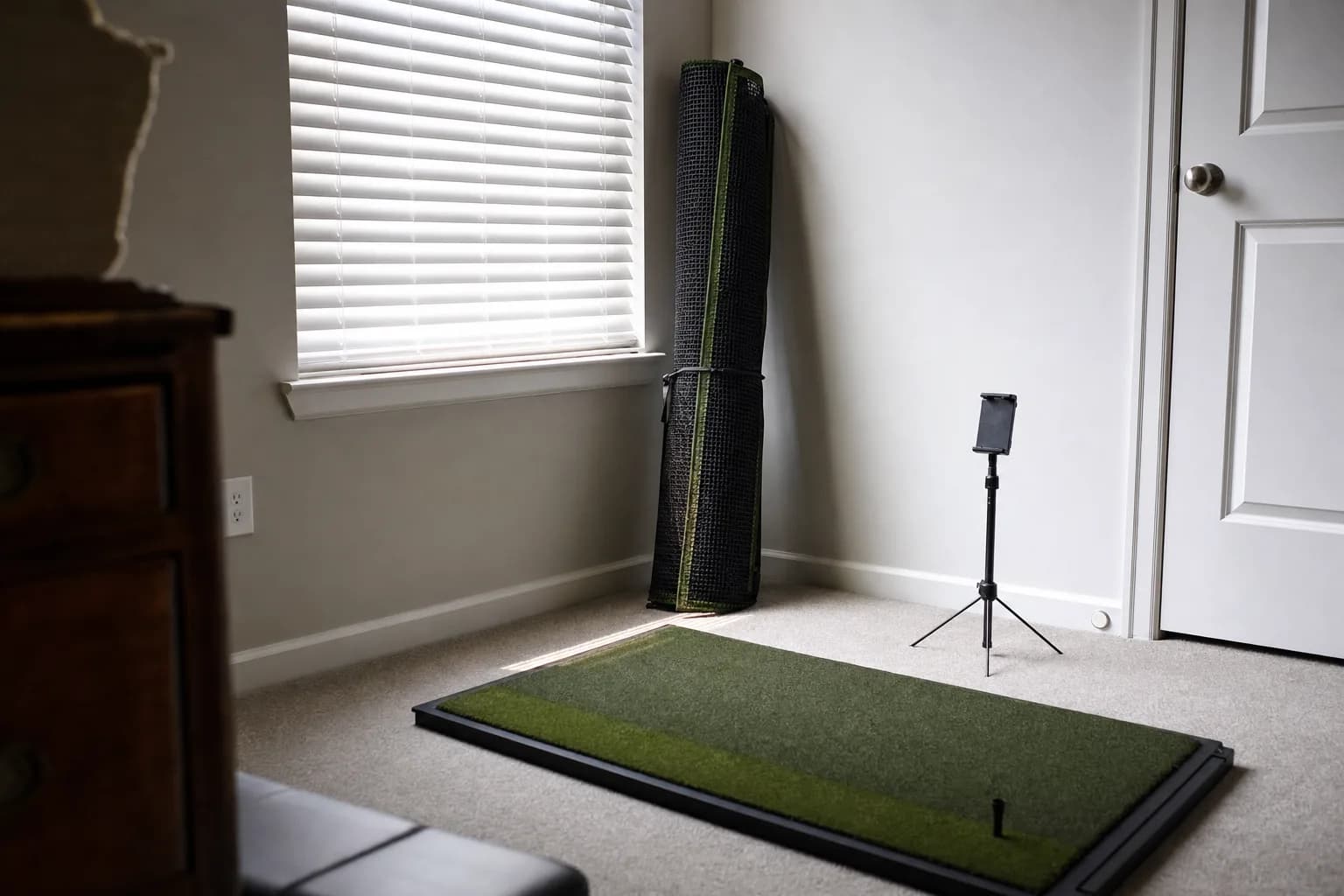 A tidy corner of a spare room set up for golf practice with a rolled-up net and a compact turf mat