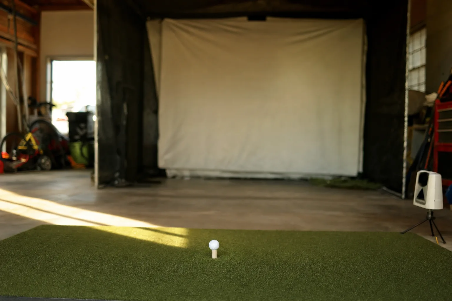 A launch monitor set up on a hitting mat in front of an impact screen