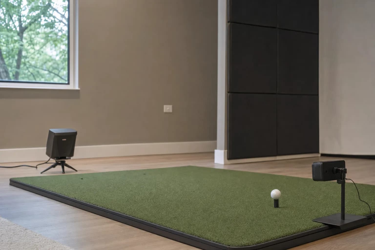 A home hitting bay with a radar-style sensor on a tripod behind the mat and a camera-style sensor on a stand beside a teed ball